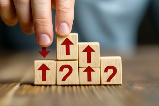 A hand arranging wooden blocks with arrows and question marks on a wooden surface in a close up view