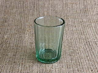 An old faceted vodka glass. In USSR it was called Granchik. An empty glass against a burlap...