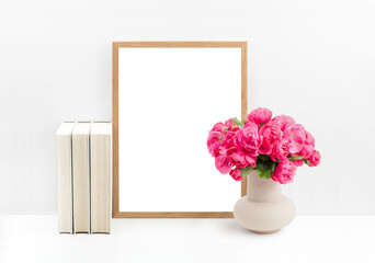 modern romantic mockup with wooden picture / photo frame, cream colored books and a bunch of roses in a vase on a white shelf or table against a bright wall, cut-out transparent space for your artwork