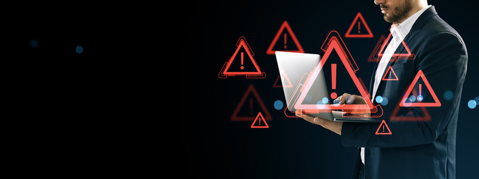 Businessman using laptop surrounded by digital red warning symbols and exclamation marks on dark background indicating cyber danger and data alerts.