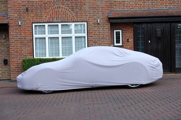 An automobile shielded by a cover is parked in front of a home