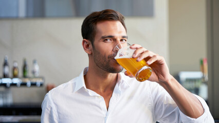 Fototapeta premium Man in white shirt drinking glass of golden beer in modern bar setting during International Beer Day