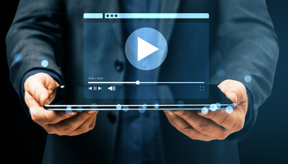 Man holding digital tablet displaying online video player interface with play button and progress bar on dark background, concept of streaming service.