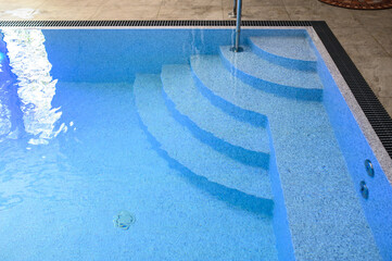 Overflow pool with clean, clear blue water. Smooth descent into the pool by steps. Vacation outside the city