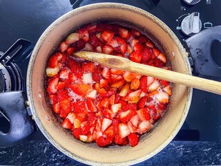 A pot of chopped strawberries cooking on a stove with a wooden spoon stirring the fruit mixture