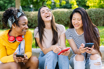 Three happy women using mobile phones at city street, laughing while watching social media content on cell app