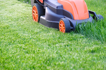 Process of mowing grass with an electric lawn mower, lawn care in the yard of  country house.