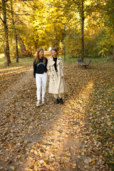 Fototapeta premium Two friends walk together in a sunny autumn park, chatting and enjoying the warm day surrounded by golden foliage.