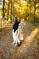 Fototapeta premium Two friends pose together in a golden autumn park, enjoying the warm light and cozy atmosphere of a beautiful day.