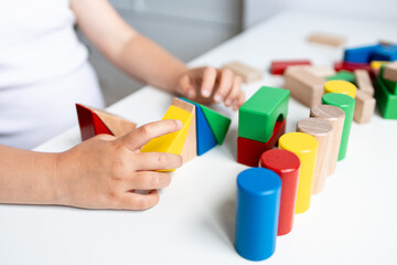 Child engaging with colorful geometric wooden blocks on white table
