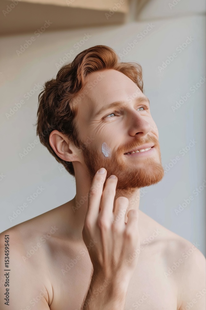Poster A man with a beard is applying lotion to his face. He is smiling and he is in a good mood