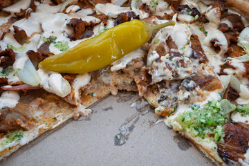 Close-up of partially eaten doner kebab pizza with creamy sauce and pickled pepper in a box