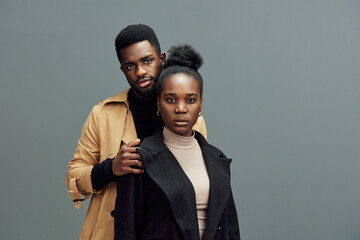 Portrait of a stylish African couple showcasing contemporary fashion in neutral tones, conveying confidence and connection against a minimalist gray backdrop