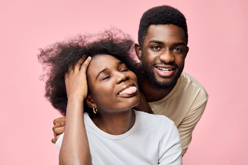 Obraz premium Happy young couple expressing joy with playful emotions on a pink background, showcasing a casual style in summer clothing and natural hairstyles