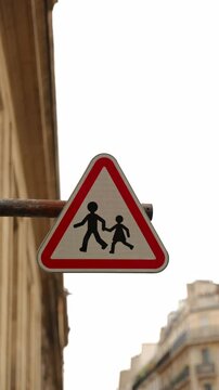 Un panneau triangulaire rouge avertit les conducteurs de la pr&eacute;sence de pi&eacute;tons et d'enfants traversant la rue, assurant la s&eacute;curit&eacute; des passants.