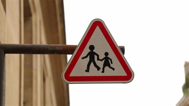 Un panneau triangulaire rouge avertit les conducteurs de la pr&eacute;sence de pi&eacute;tons et d'enfants traversant la rue, assurant la s&eacute;curit&eacute; des passants.
