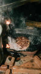 A grill is cooking a burger and the smoke is rising. The burger is brown and has grill marks