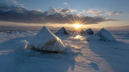 A tranquil winter landscape with snow-covered ice sculptures of pyramids illuminated by the golden rays of the rising sun over endless expanses of frozen water.