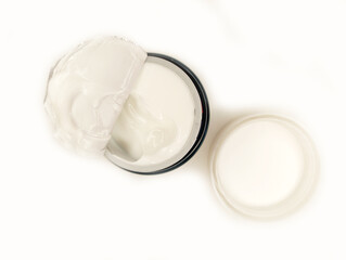 Cream container with a lid partially open displaying smooth white cream on a plain background