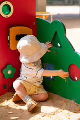 Baby boy dressed with summer cloves and hat is playing outside on the street, touching and exploring playground for little ones. Learning  numbers and shapes.