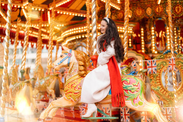 Woman riding a beautifully decorated carousel horse while wearing a stylish outfit, enjoying a festive atmosphere at an amusement park during daytime © Iryna