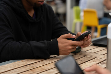 People using smartphones in a casual environment with wooden tables and colorful seating during daytime social gathering