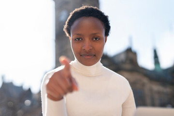 Confident individual pointing forward with intensity in a sunny urban setting, showcasing...