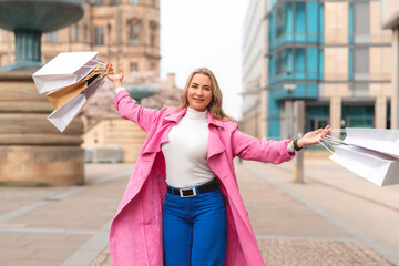 Woman enjoying a shopping day in a stylish pink coat with shopping bags in a cityscape during spring