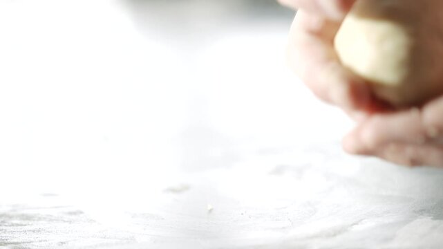 A person is kneading dough on a counter. The dough is white and he is a type of bread. The person's hands are covered in flour, and they are working to shape the dough into a round ball