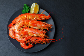 Fried shrimps on a plate with piece of lemon on black background. Flat lay, copy space.