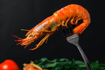 Grilled shrimp on a fork on black background fresh vegetables on back. Close up.