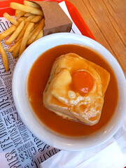 Traditional Portuguese Francesinha Sandwich with Melted Cheese and Fried Egg in Rich Beer Sauce