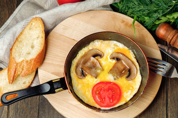 Omelet with mushrooms and tomato with pieces of bread in a pan on wooden background. Rustic...