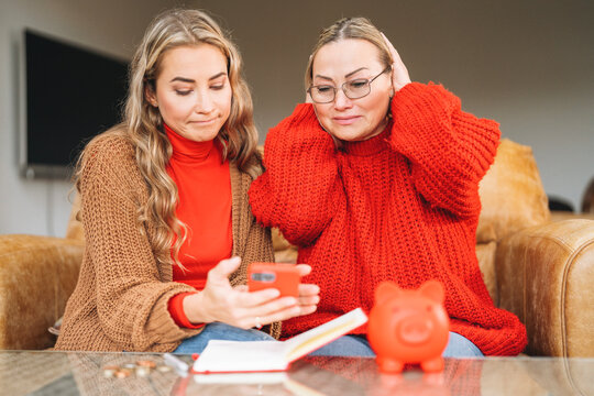 Two women looking at a smartphone while seated in a cozy living room during a casual gathering focusing on personal finance tips