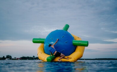 Młodzieżowa zabawa podczas wakacji na letnim obozie sportowym na dmuchanej kuli, atrakcja na wodzie z siłowaniem i zwinnością