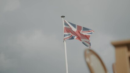 A flag with the British Union Jack is flying in the sky. The flag is red, white, and blue - Powered by Adobe