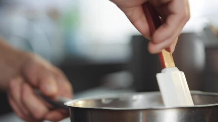 A person is stirring a pot with a white spatula. The person is wearing a red glove
