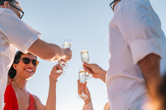 Happy Caucasian people enjoy celebration party drinking champagne on luxury catamaran boat yacht in the sea on summer beach holiday vacation. Man and woman travel nature ocean on cruise ship at sunset