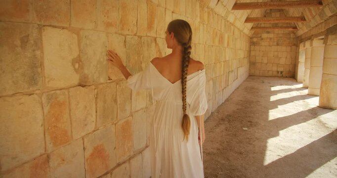 Female tourist touching historic stone wall inside archaeological structure of Mayan ruins
