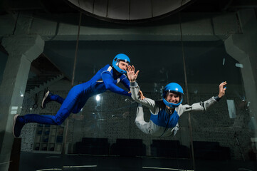 A male instructor teaches a woman how to fly in a wind tunnel. Free fall simulator.