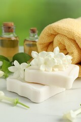 Bars of soap, jasmine flowers and towel on white marble table, closeup