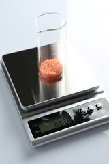 Laboratory scale with beaker of sample on white background, closeup