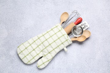 Different kitchen utensils in oven mitten on light table, top view