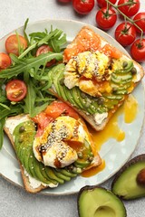 Delicious sandwiches with avocado, poached egg, salmon, tomatoes and arugula on gray table, flat lay