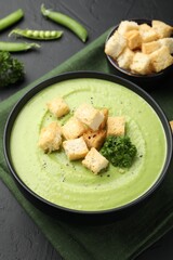 Tasty pea cream soup with croutons and broccoli served on black table, closeup