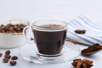 Cup of aromatic coffee, beans and star anise on white table, closeup