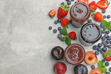 Different sweet jams in jars and ingredients on grey table, flat lay. Space for text