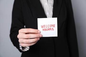 Human resources manager holding sticky note with words Welcome Aboard on grey background, closeup