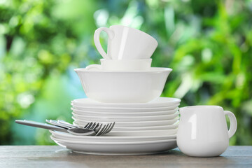 Different clean dishes on wooden table against blurred green background