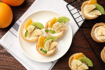 Tartlets with fruits and mint on wooden table, flat lay. Delicious dessert